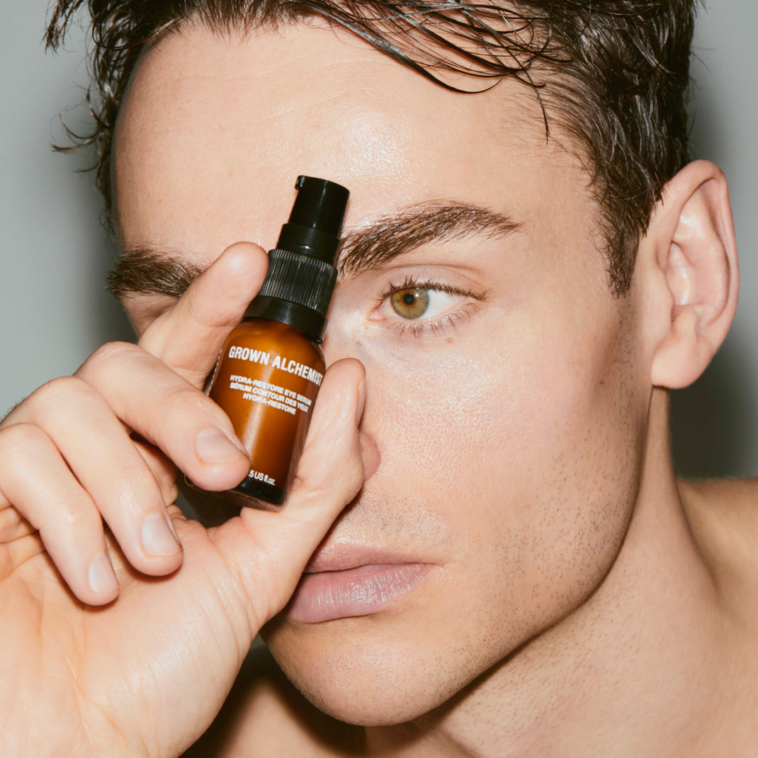 Person holding a bottle of 'Grown Alchemist' product near their face against a neutral background