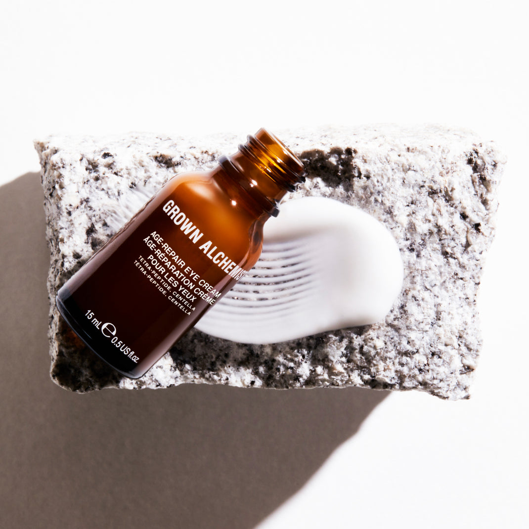 Brown bottle of Grown Alchemist eye cream on a textured stone surface with a white background