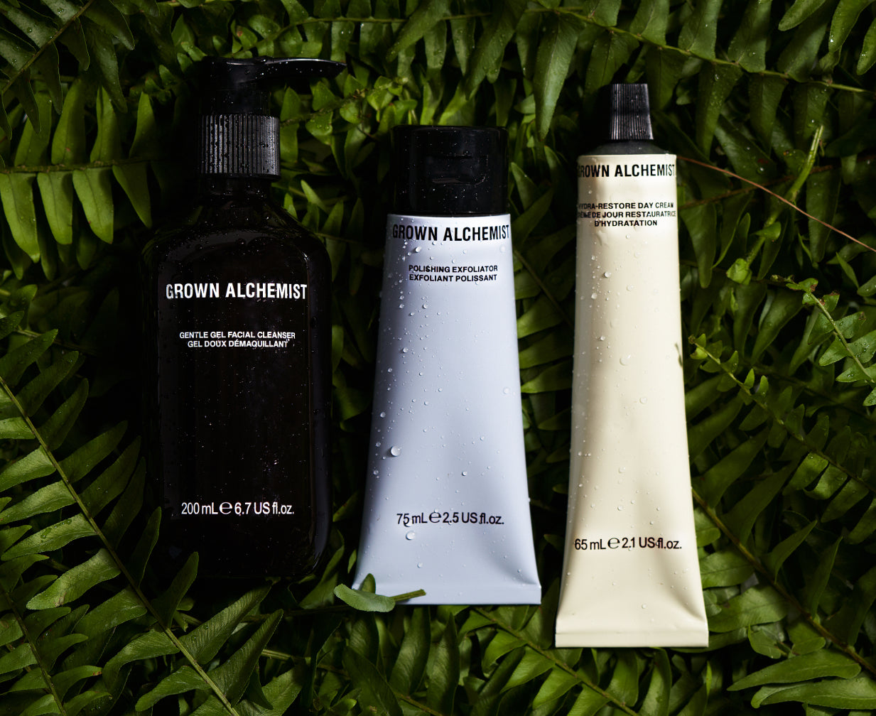 Three Grown Alchemist skincare products on a green leaf background