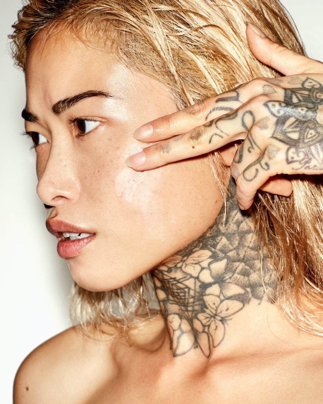 Close-up of a person with tattoos on their neck and face against a plain background