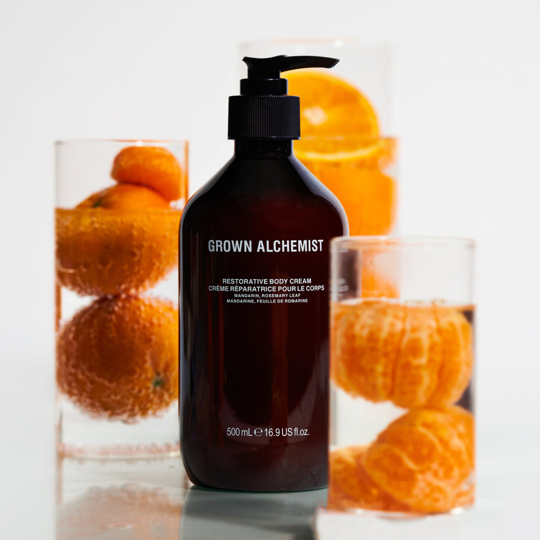 Grown Alchemist body cream bottle with oranges in the background