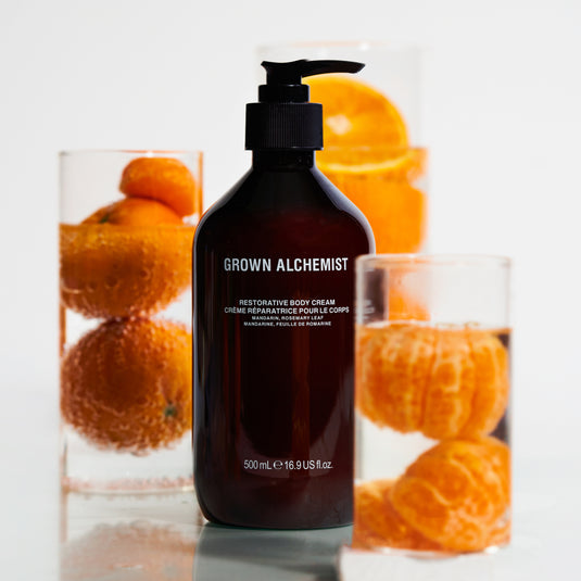 Grown Alchemist body cream bottle with oranges in the background
