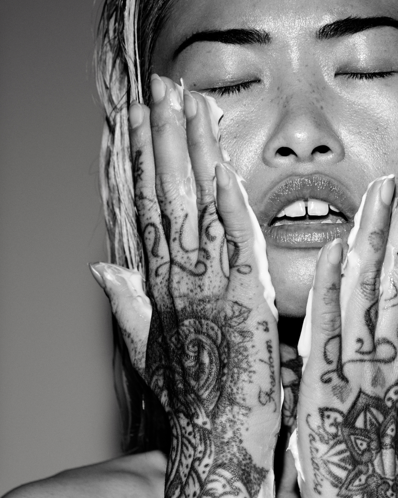 Black and white close-up of a person with tattoos on their hands, covering their face.