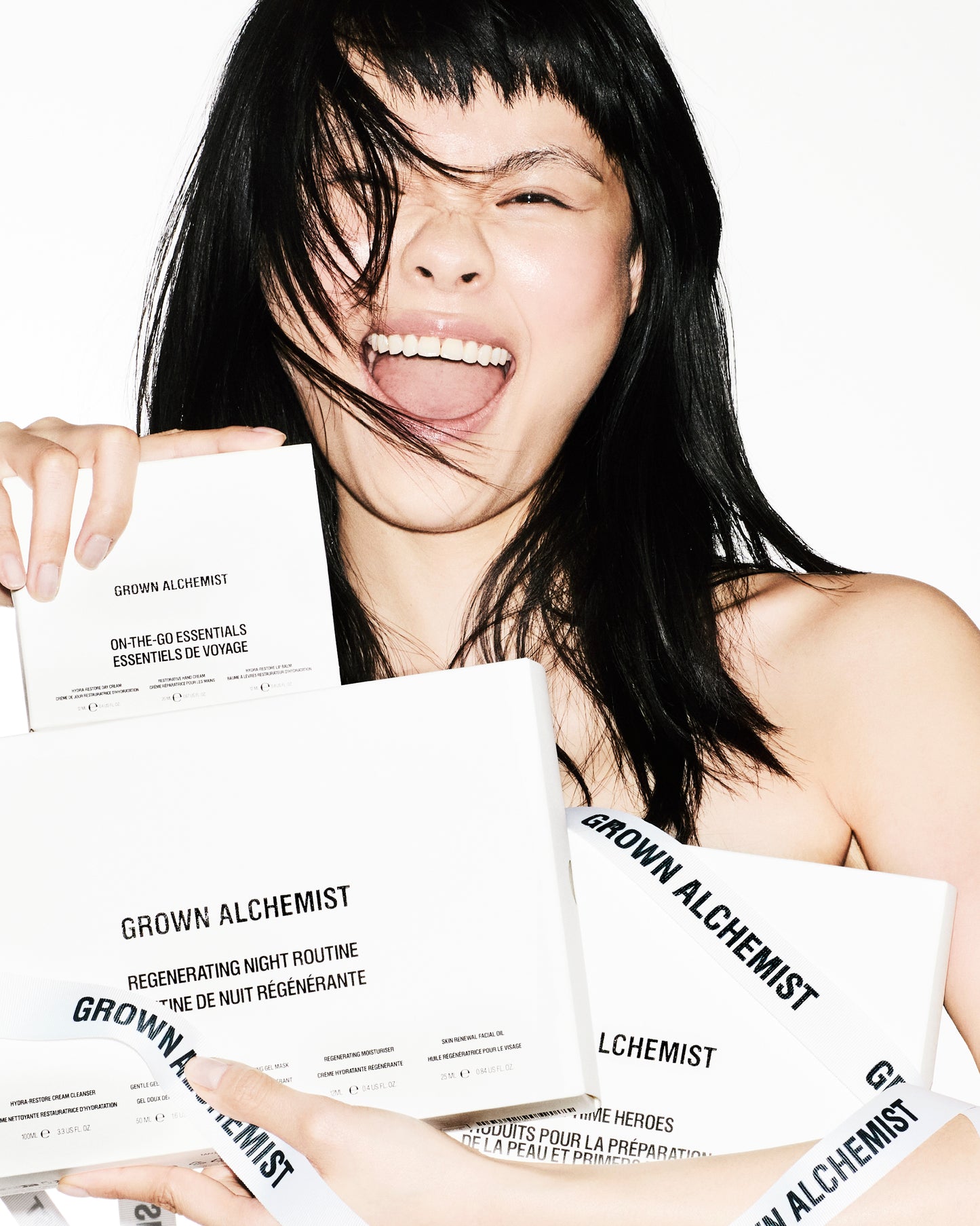 Woman holding Grown Alchemist skincare products with a white background