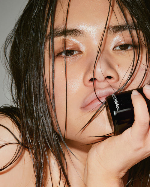 Person applying makeup with a brush to their face against a neutral background