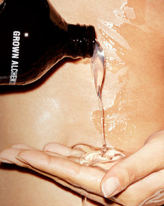 Hand pouring a clear liquid from a bottle labeled 'Grown Alchemist' onto skin.