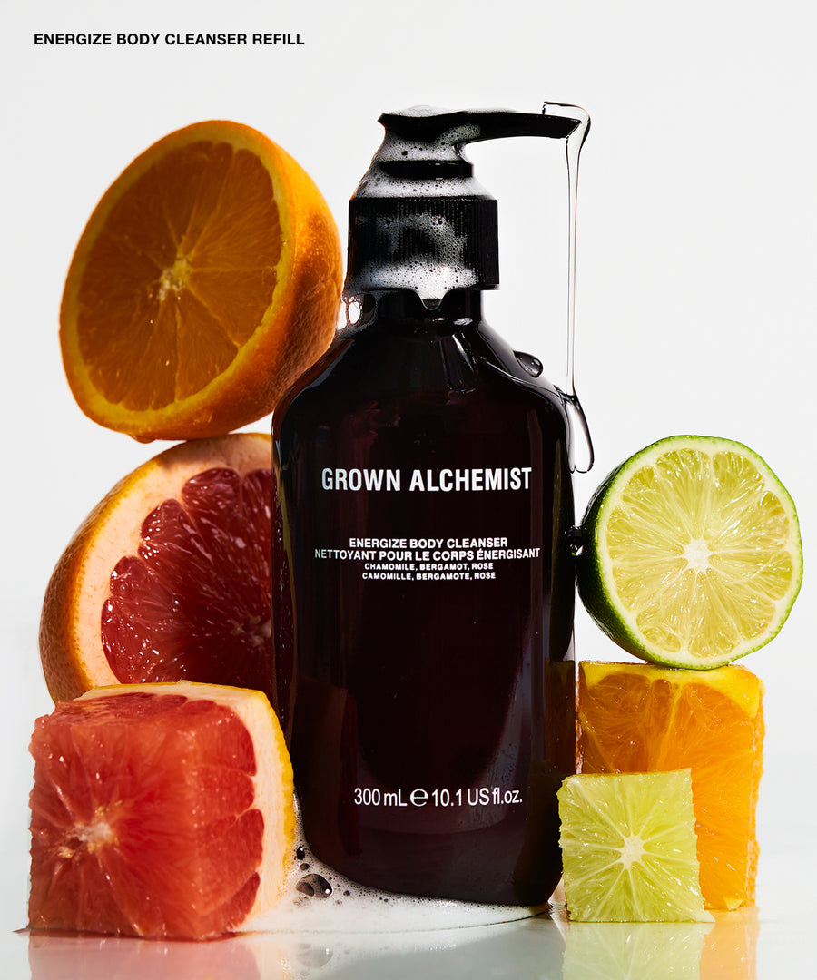 A bottle of Grown Alchemist Energize Body Cleanser Refill surrounded by fresh citrus fruits including orange, grapefruit, and lime slices on a white background.