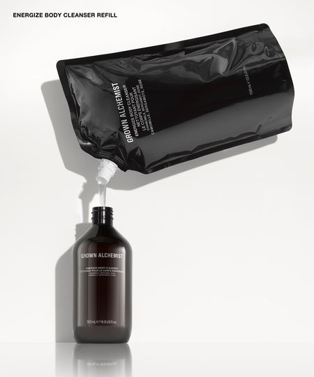 A black refill pouch labeled 'GROWN ALCHEMIST' pouring a liquid into a dark amber bottle also labeled 'GROWN ALCHEMIST' on a clean white background.