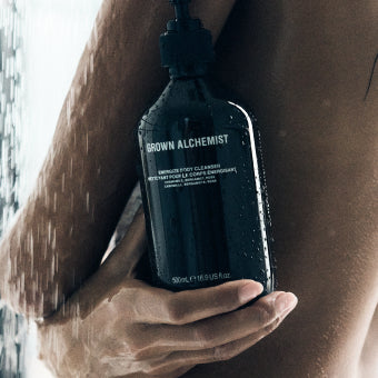 Hand holding a bottle of 'Grown Alchemist' product against their body with a blurred background