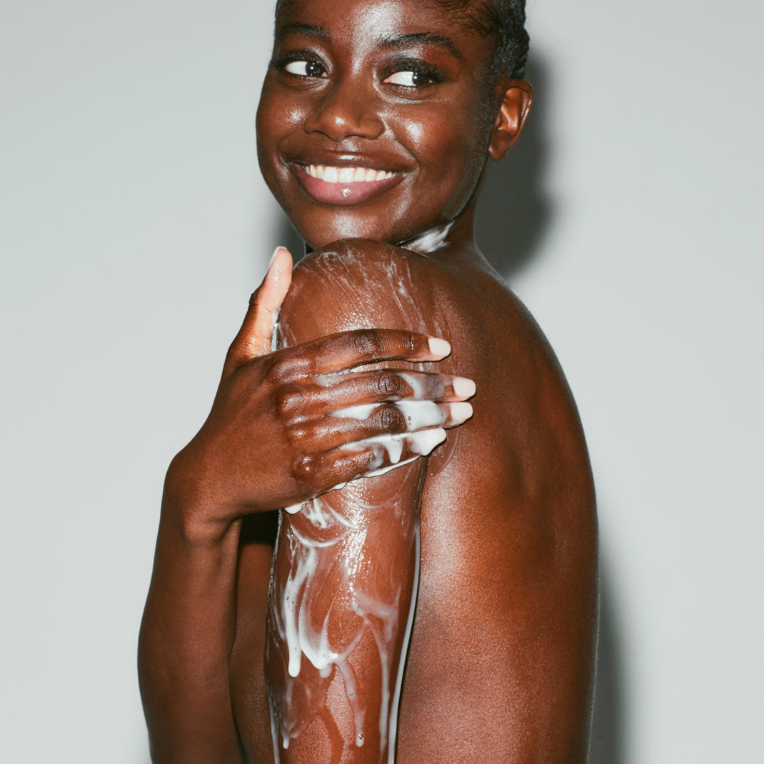 Woman applying sunscreen to her shoulder with a neutral background