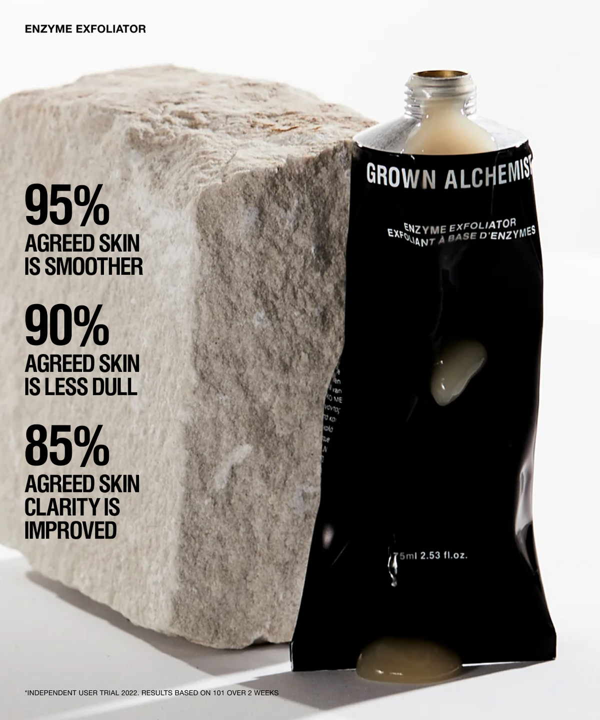 A black squeeze tube of GROWN ALCHEMIS Enzyme Exfoliator stands against a large rough stone on a white studio background, with marketing text on the left describing skin benefits.