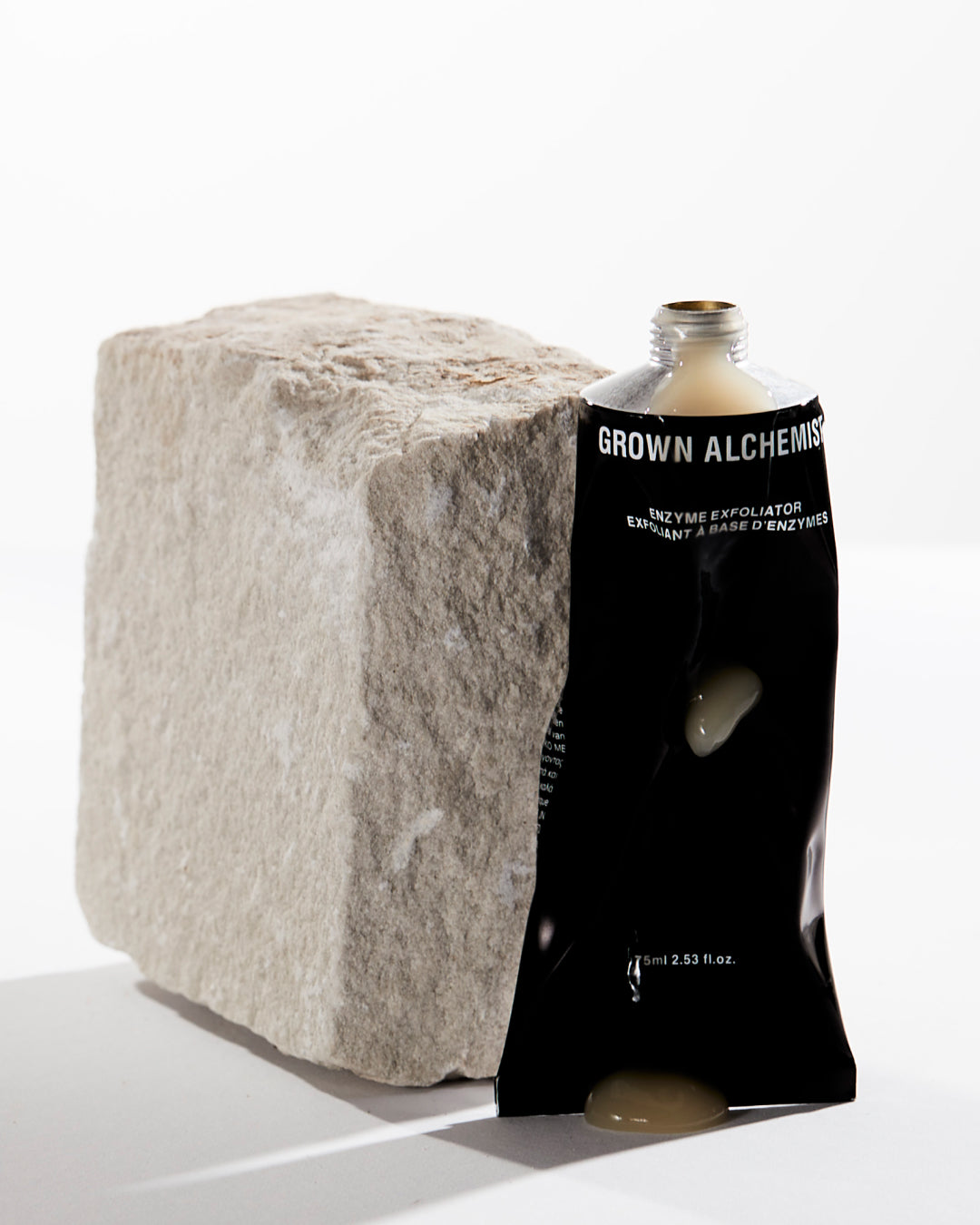 Black 'Grown Alchemist' tube next to a textured stone block on a white background