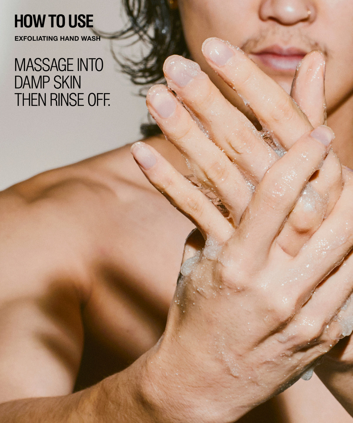 Close-up of a person's hands lathering with exfoliating hand wash, with overlaid text reading 'HOW TO USE' and 'MASSAGE INTO DAMP SKIN THEN RINSE OFF.'.