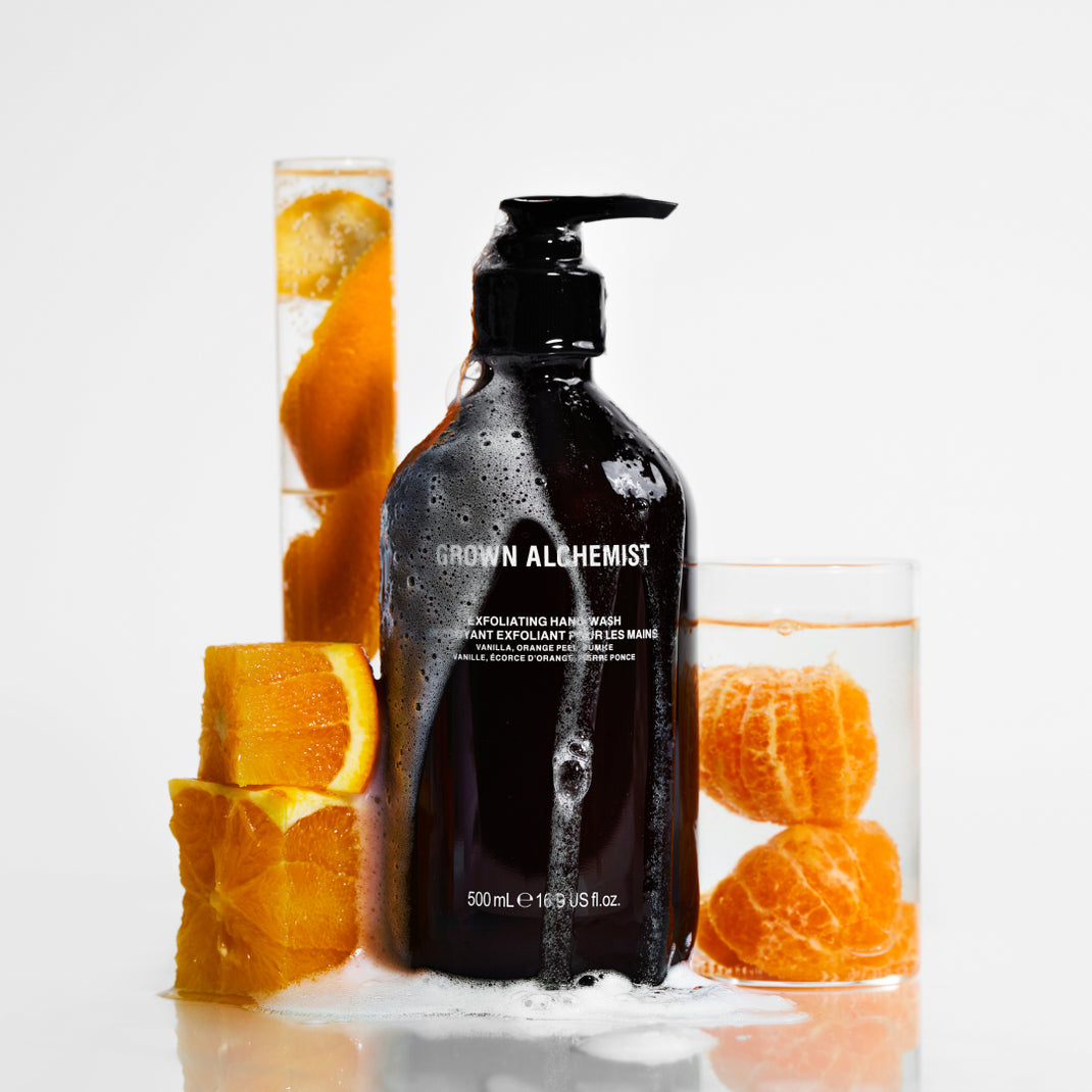 Bottle of Exfoliating Hand Wash with oranges and a glass container on a white background