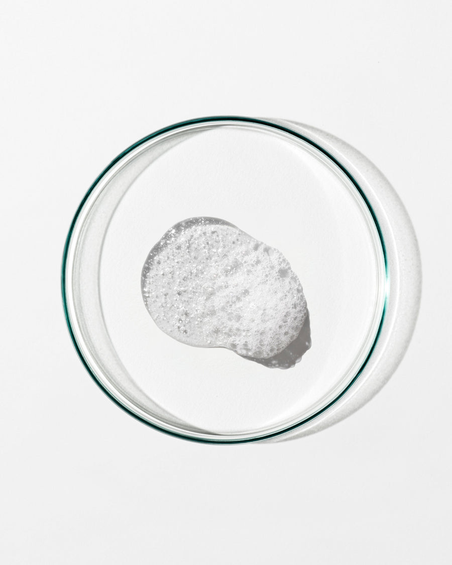Clear petri dish with a small amount of white foam on a white background