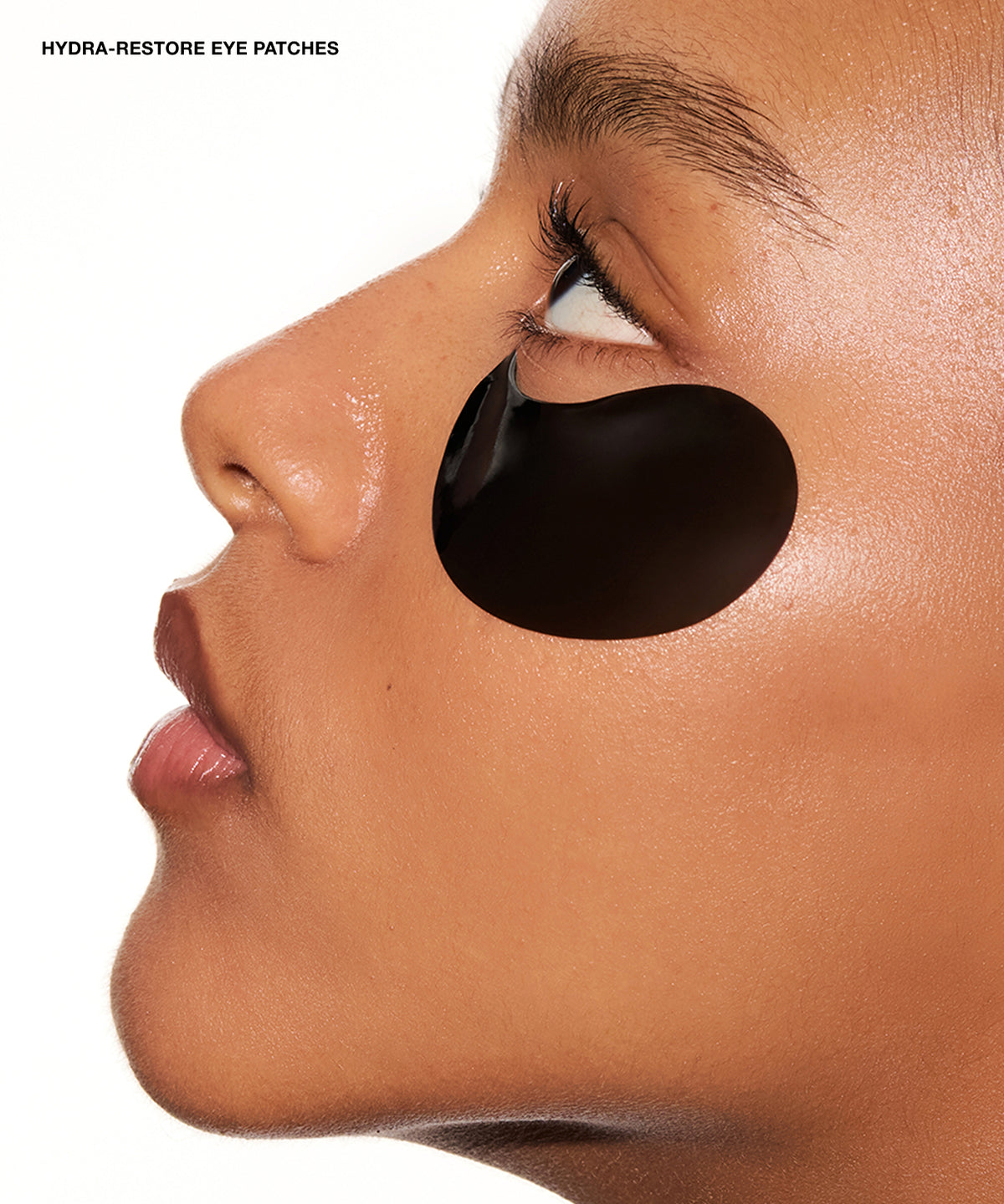Close-up side profile of a person wearing a black oval eye patch under the eye, with the text 'HYDRA-RESTORE EYE PATCHES' in the top left corner on a white background.