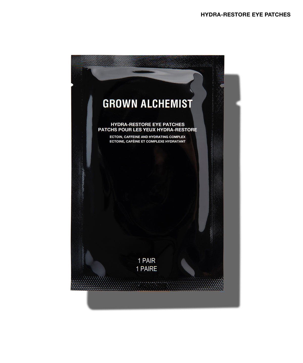 A single black Grown Alchemist Hydra-Restore Eye Patch sachet on a white background with a soft shadow.