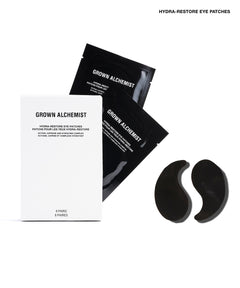 Grown Alchemist Hydra-Restore Eye Patches shown with their white and black packaging on a clean white background. The set includes two black crescent-shaped eye patches and their corresponding boxes.
