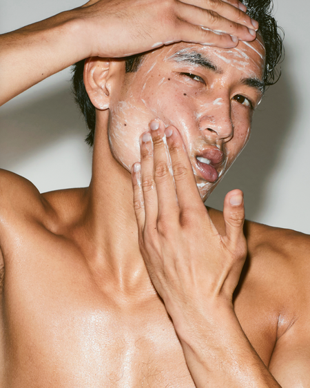 Man applying cream to his face with a neutral background