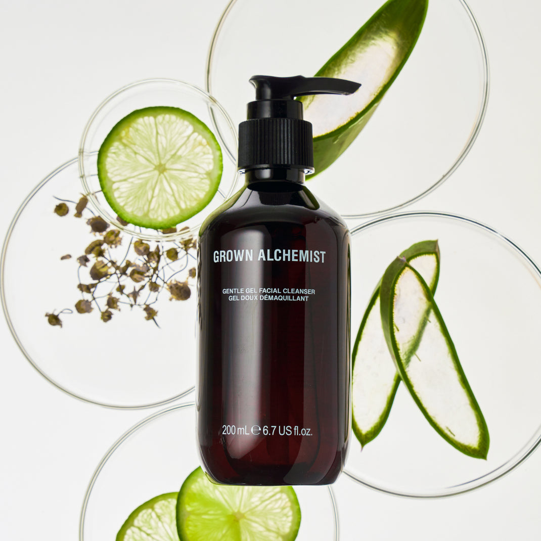 Pump bottle of Grown Alchemist product on top of clear dishes containing ingredients