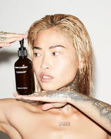 Person holding a bottle of 'Grown Alchemist Gentle Gel Facial Cleanser' product with a neutral background