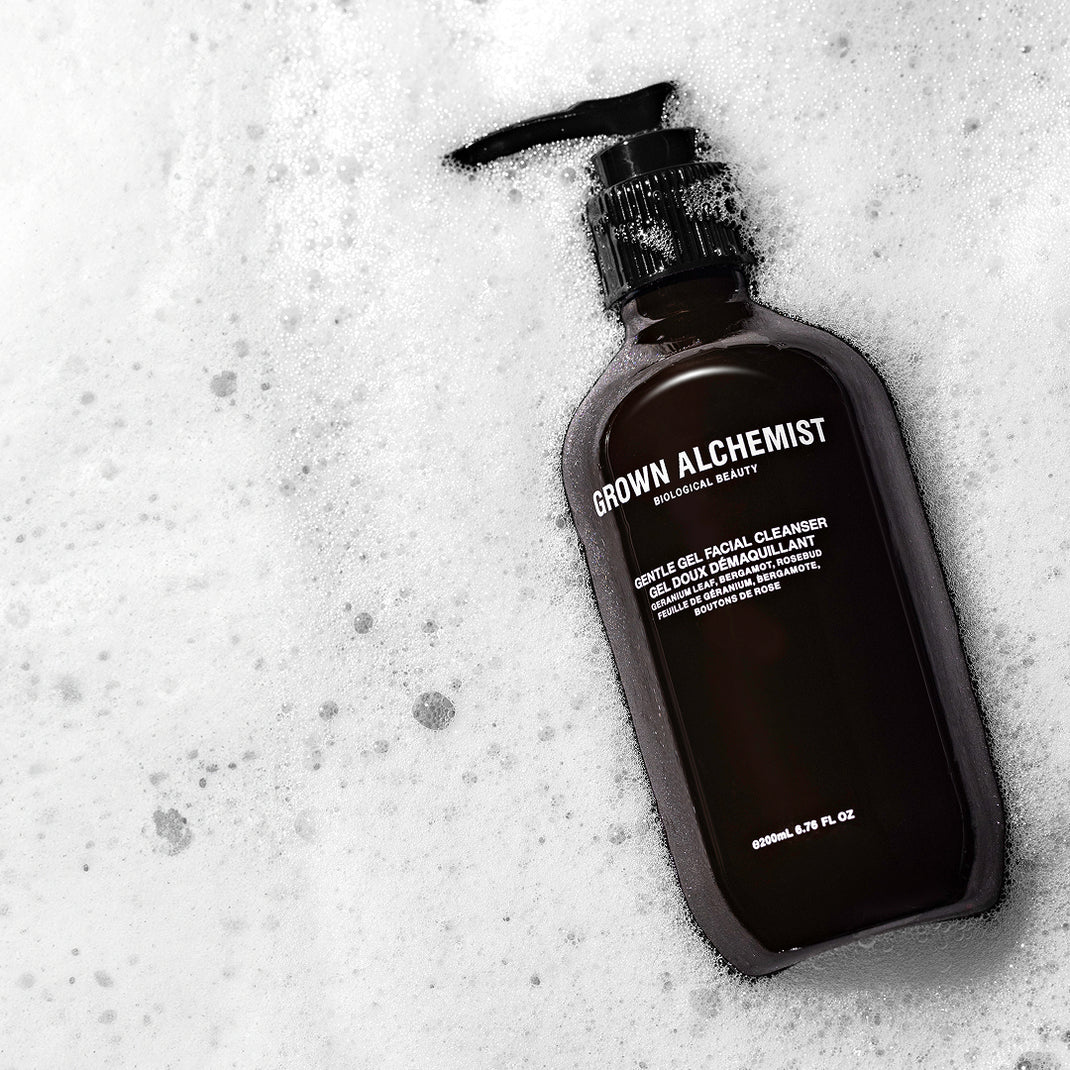 Bottle of Grown Alchemist facial cleanser on a foamy white background