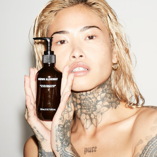 Person holding a bottle of 'Grown Alchemist' product against a plain background
