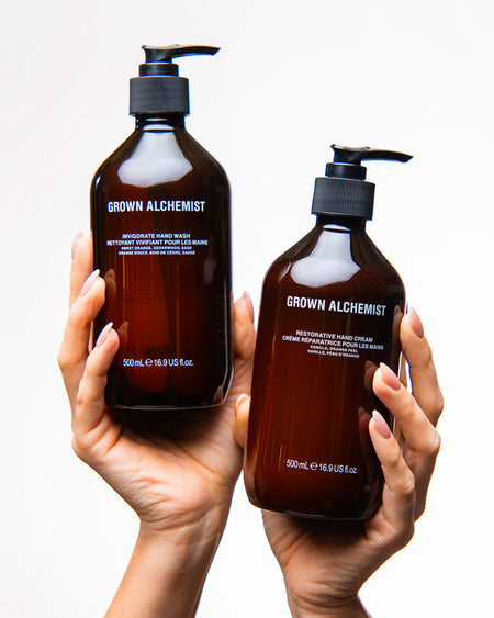 Two bottles of Grown Alchemist hand wash and cream held in hands against a white background