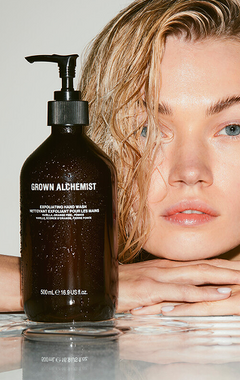Grown Alchemist exfoliating hand wash bottle with a person leaning on a reflective surface