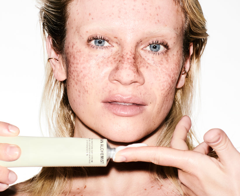 Person holding a skincare product with a close-up of her face showing freckles.