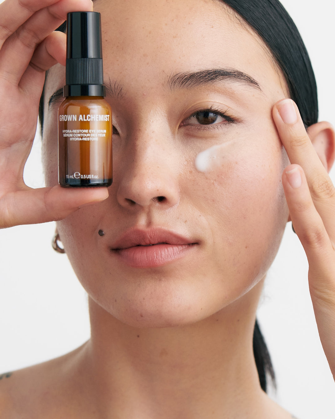 Person applying skincare product with a bottle labeled 'Grown Alchemist' on a neutral background