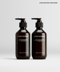 Two dark amber pump bottles of Grown Alchemist Hydra-Restore Conditioner on a light gray background.