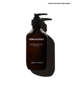A dark amber pump bottle of Grown Alchemist Hydra-Restore Conditioner on a white background with a strong cast shadow.