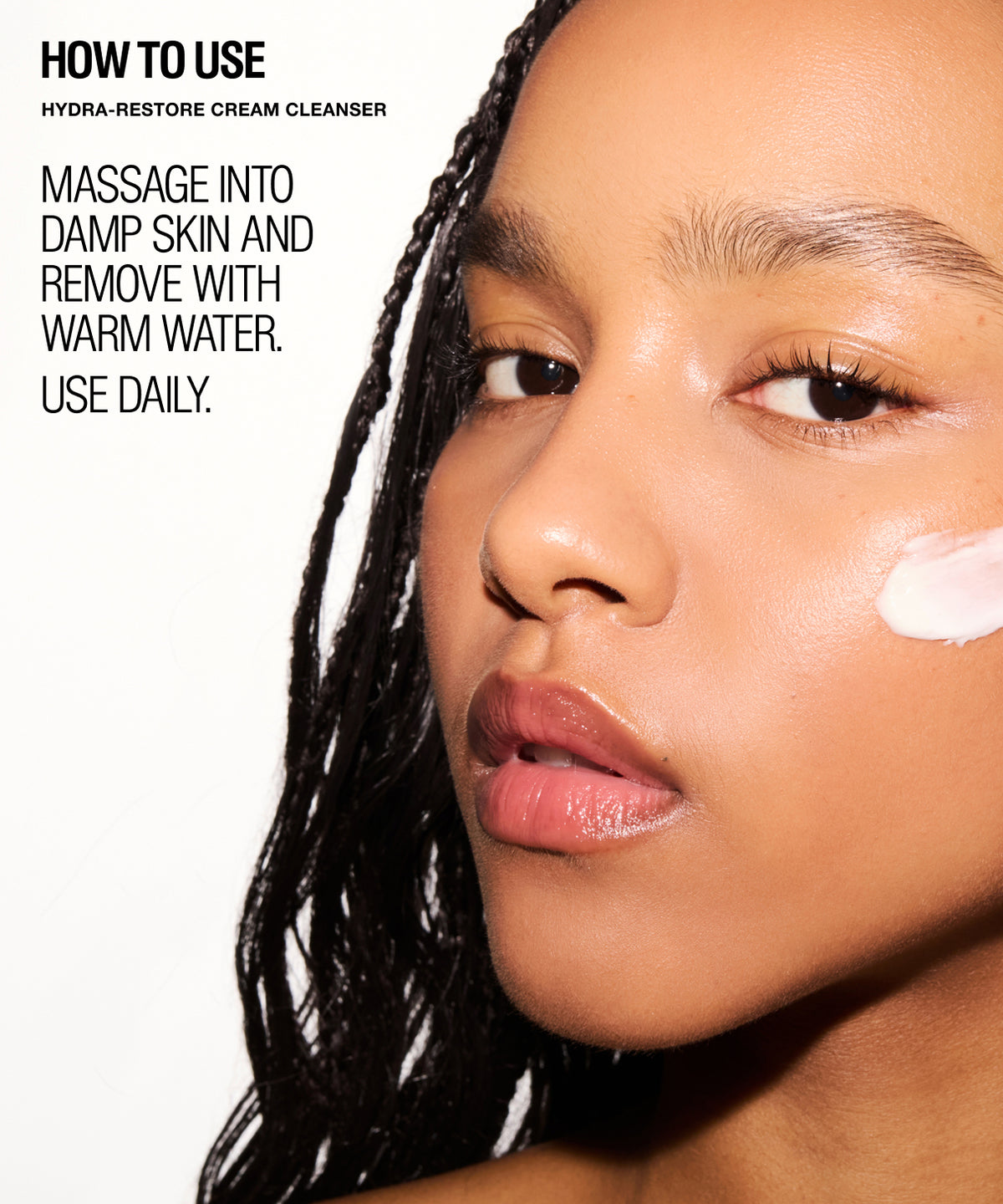 Close-up beauty ad showing part of a woman's face with text reading 'HOW TO USE HYDRA-RESTORE CREAM CLEANSER' and instructions on how to apply the cleanser. A white cream swatch is visible on her cheek against a clean white background.