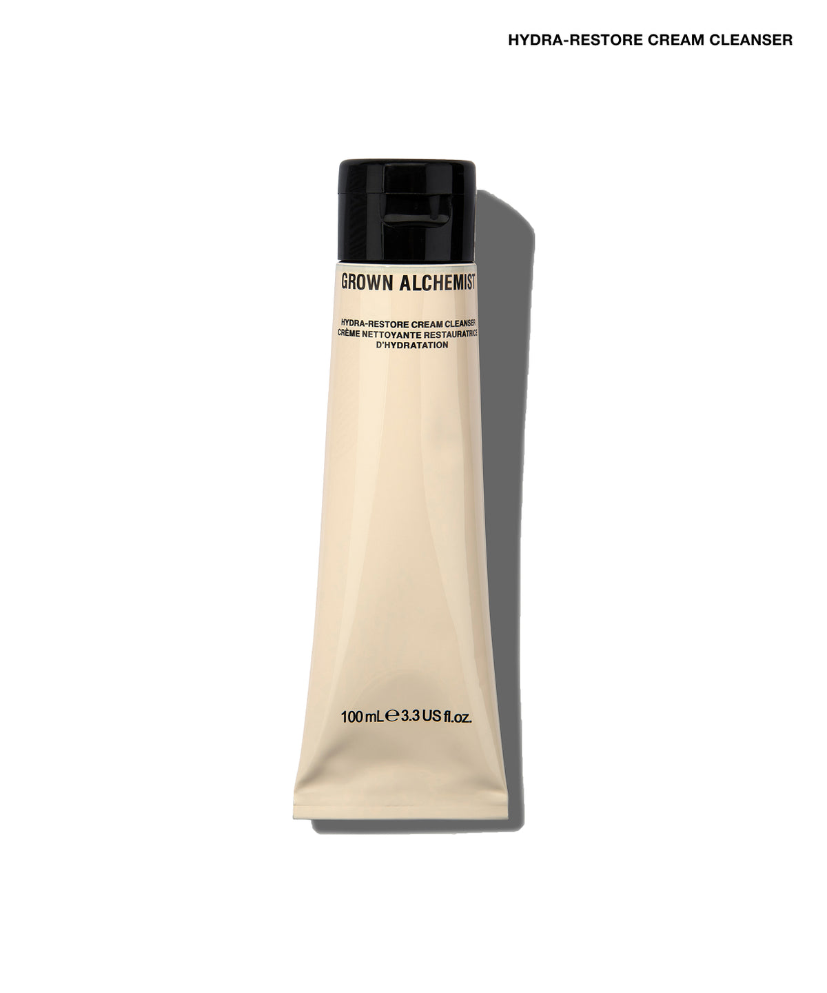 A squeeze tube of Grown Alchemist Hydra-Restore Cream Cleanser on a clean white background with a soft shadow. The tube is a warm cream color with a black cap, and the brand name is printed in black text on the front.