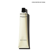A squeeze tube of Brown Alchemy Hydra-Restore Day Cream in a warm cream color with a black cap, shown against a white background with a soft shadow.