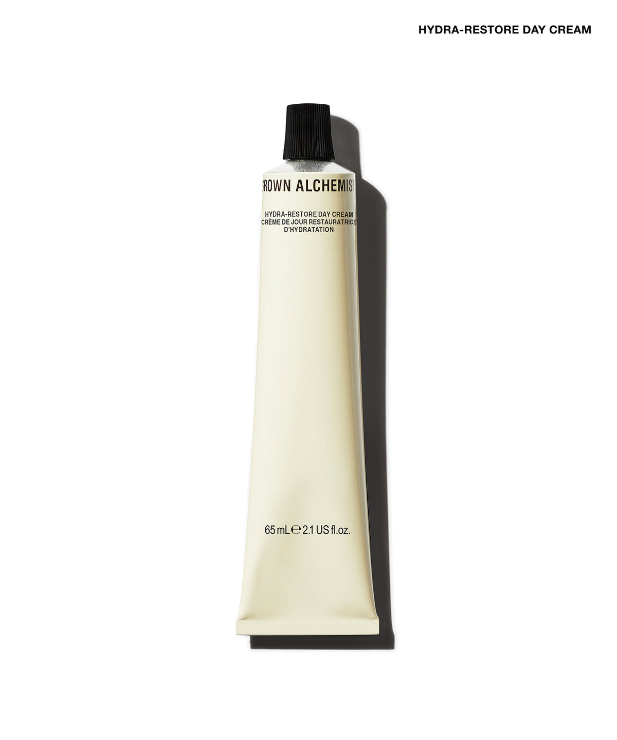 A squeeze tube of Brown Alchemy Hydra-Restore Day Cream in a warm cream color with a black cap, shown against a white background with a soft shadow.
