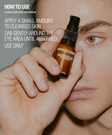 A close-up lifestyle shot of a person holding a small brown bottle of Brown Alchemy Hydra-Restore Eye Serum near their face, with white text on the left explaining how to use the eye serum.
