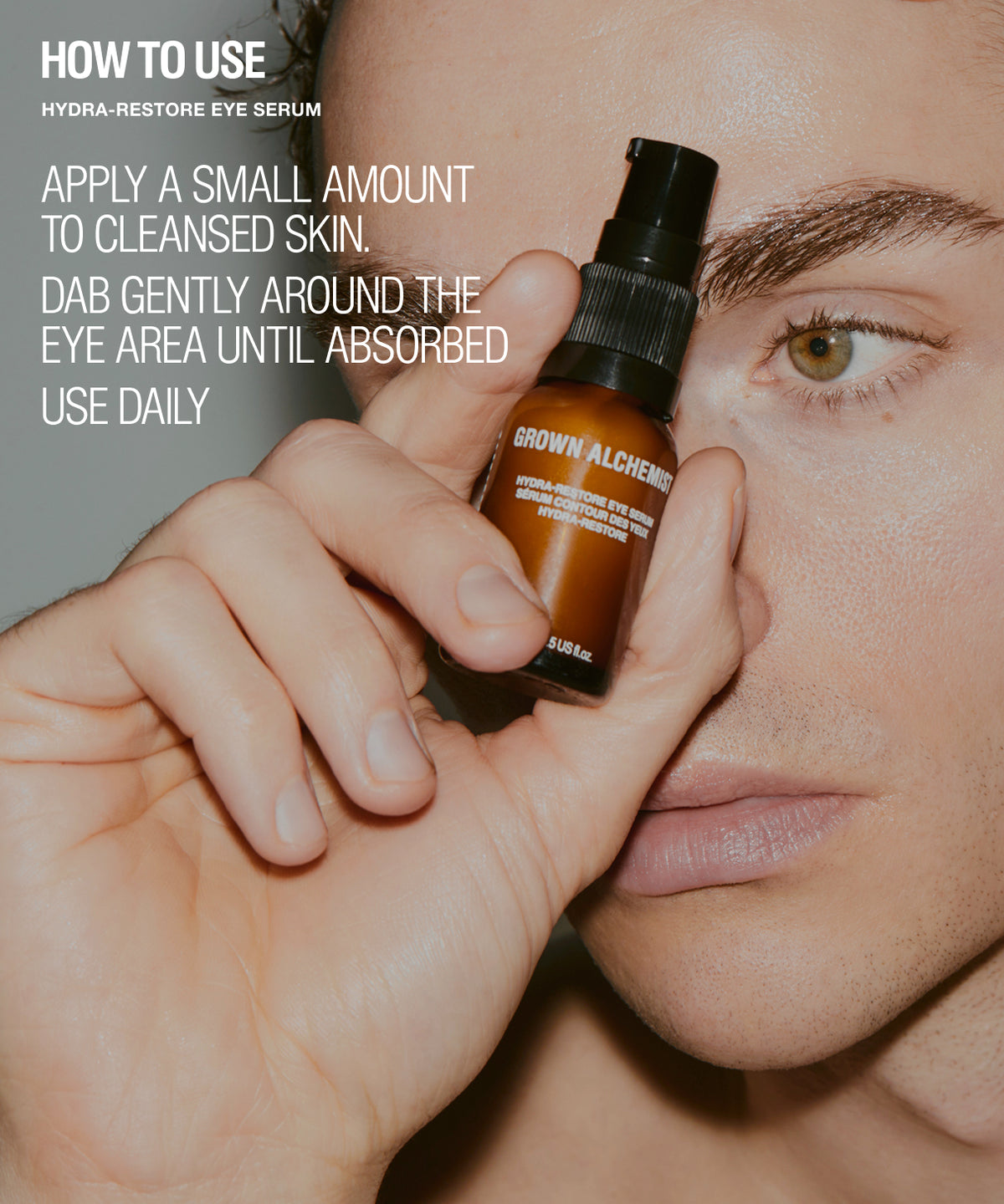 A close-up lifestyle shot of a person holding a small brown bottle of Brown Alchemy Hydra-Restore Eye Serum near their face, with white text on the left explaining how to use the eye serum.