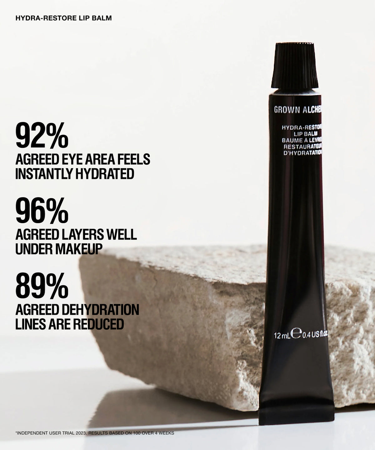 A black tube of GROWN ALGORITHM HYDRA-RESTORE LIP Balm stands upright on a light surface beside a rough stone, with large marketing text on the left describing hydration and makeup performance.