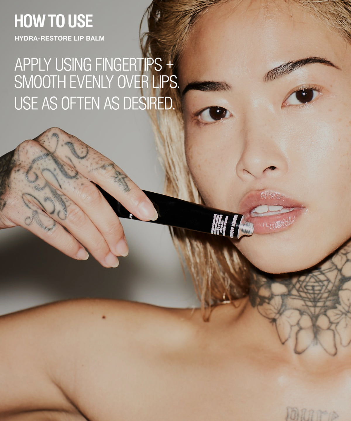 Close-up beauty shot of a woman applying a black tube of lip balm to her lips, with white text reading 'HOW TO USE HYDRA-RESTORE LIP BALM' on the left side.