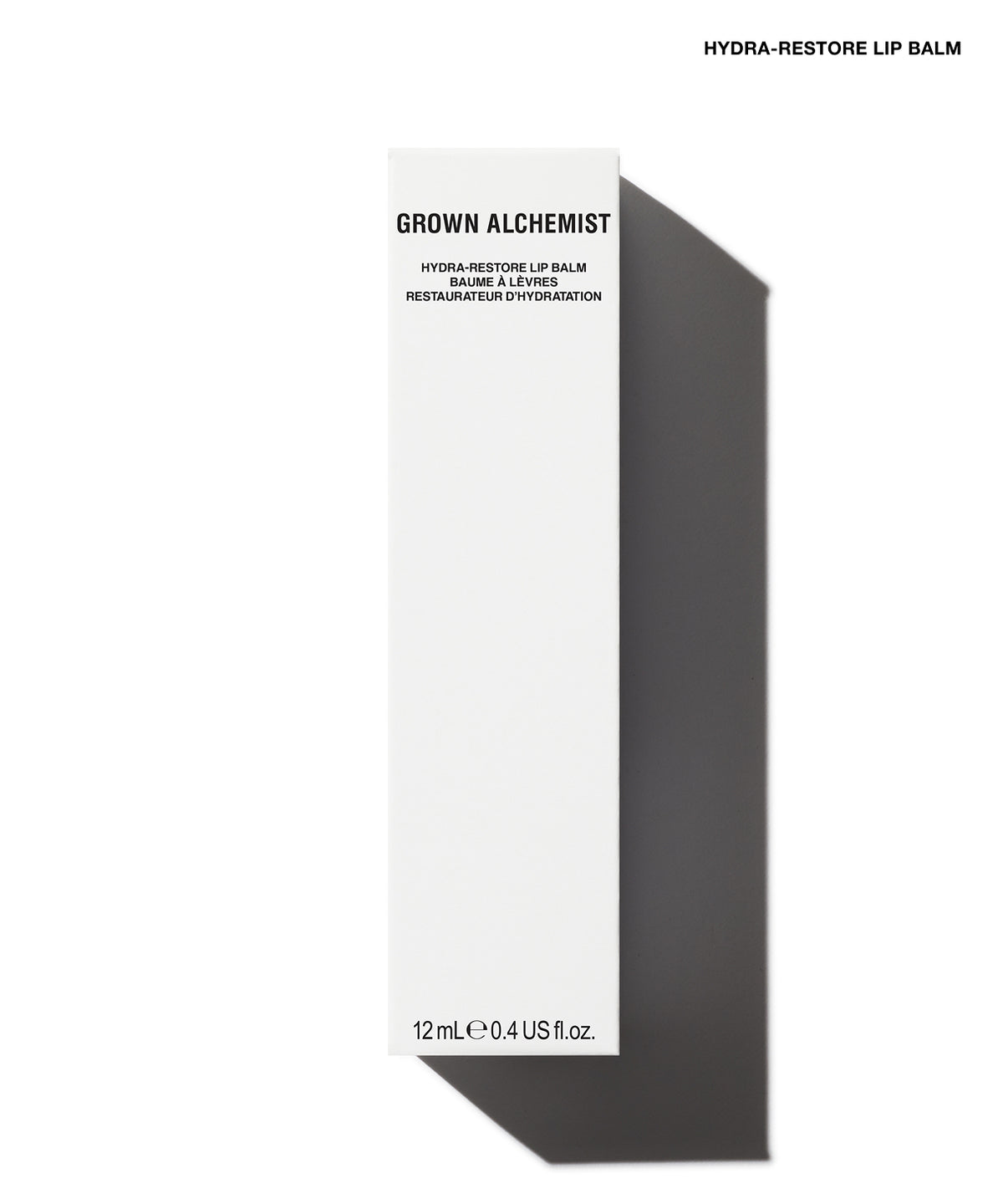 A tall, narrow white box for Grown Alchemist Hydra-Restore Lip Balm, shown on a white background with a dark gray shadow. The box features black text and is positioned vertically.
