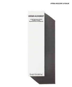 A tall, narrow white box for Grown Alchemist Hydra-Restore Lip Balm, shown on a white background with a dark gray shadow. The box features black text and is positioned vertically.