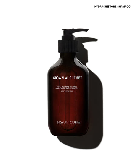 A 300mL dark amber glass pump bottle of Grown Alchemist Hydra-Restore Shampoo, shown on a white background with a dramatic shadow.