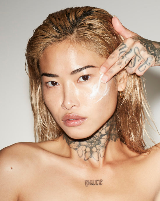 Person with tattoos on neck and arm, applying a clear face mask.