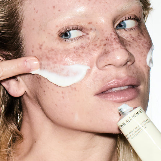Person applying cream to their face with a brand name visible