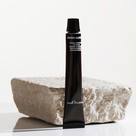 Black tube of Grown Alchemist product on a stone block with a white background