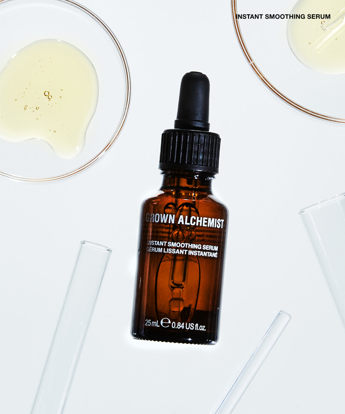 An amber glass dropper bottle labeled 'BROWN ALCHEMIST' and 'INSTANT SMoothing SERUm' is centered on a white background with glassware and serum pools around it.