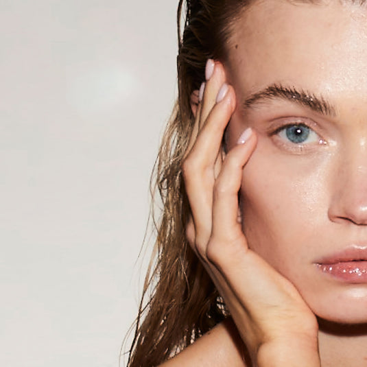 Close-up of a woman's face with one hand touching her cheek against a neutral background