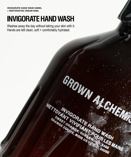 A close-up of a dark amber hand wash bottle with water droplets, featuring white text that reads 'GROWN ALCHEMY' and 'INVIGORATE HAND WASH'. The background is white with black text detailing the product's restorative cream goal and benefits.
